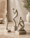Set of three abstract human figure sculptures on travertine surface with greenery