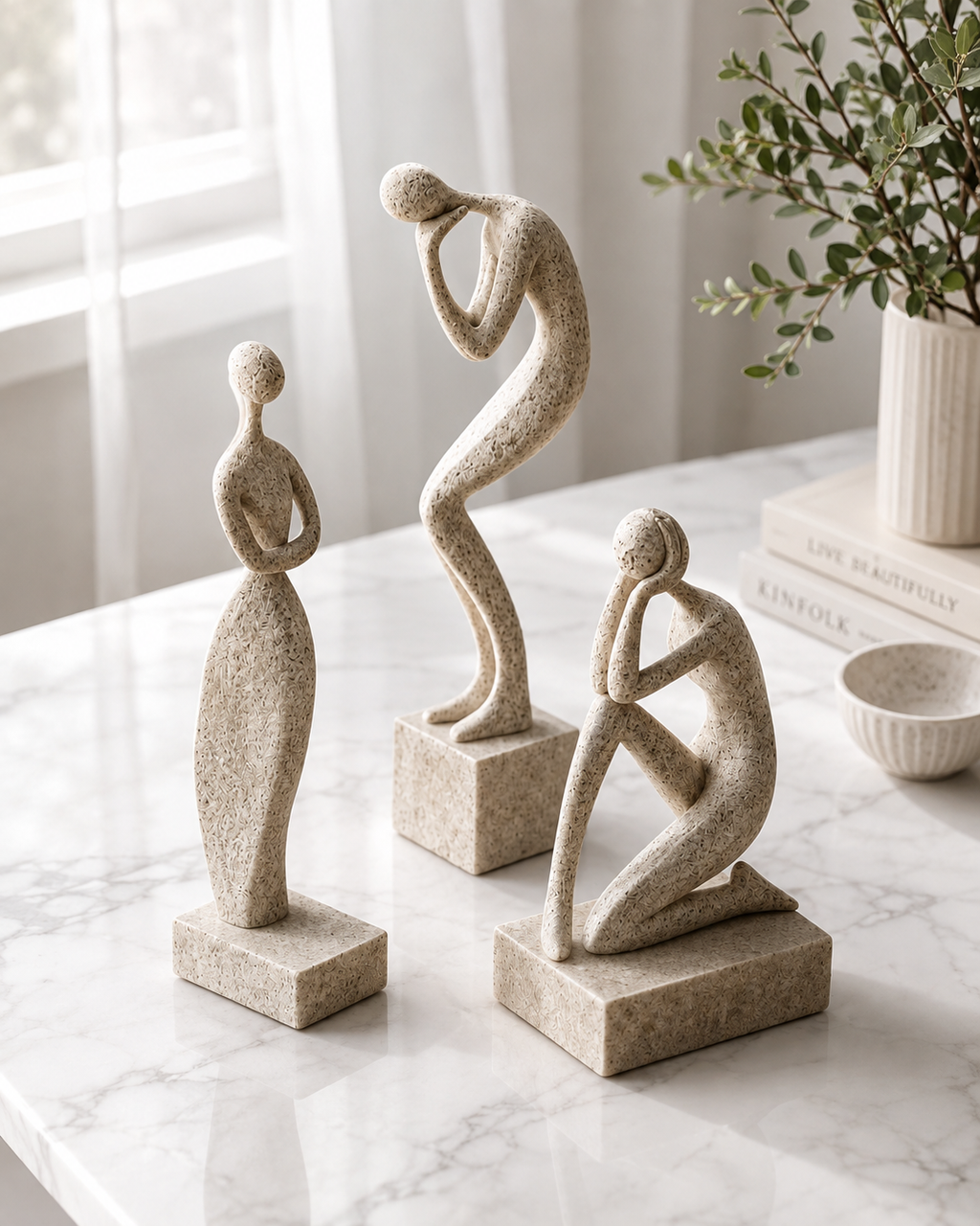 Abstract human figure sculptures on marble table with white curtain background