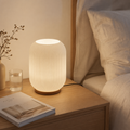 Ribbed glass table lamp glowing on wooden bedside table
