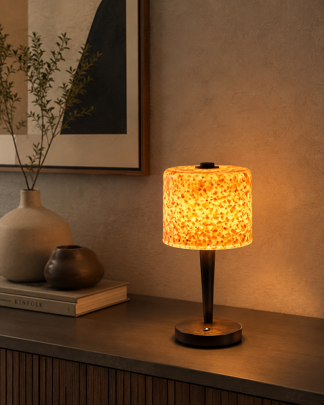 Amber terrazzo lamp on dark ribbed sideboard with ceramic vases and books