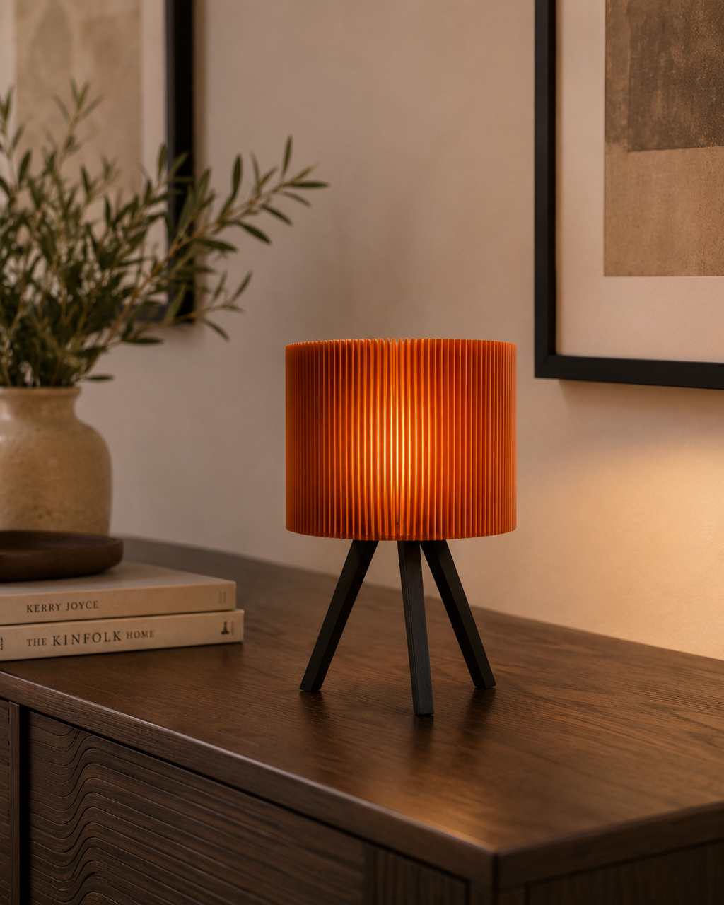 Pleated orange drum lamp on dark wooden sideboard with books and olive plant