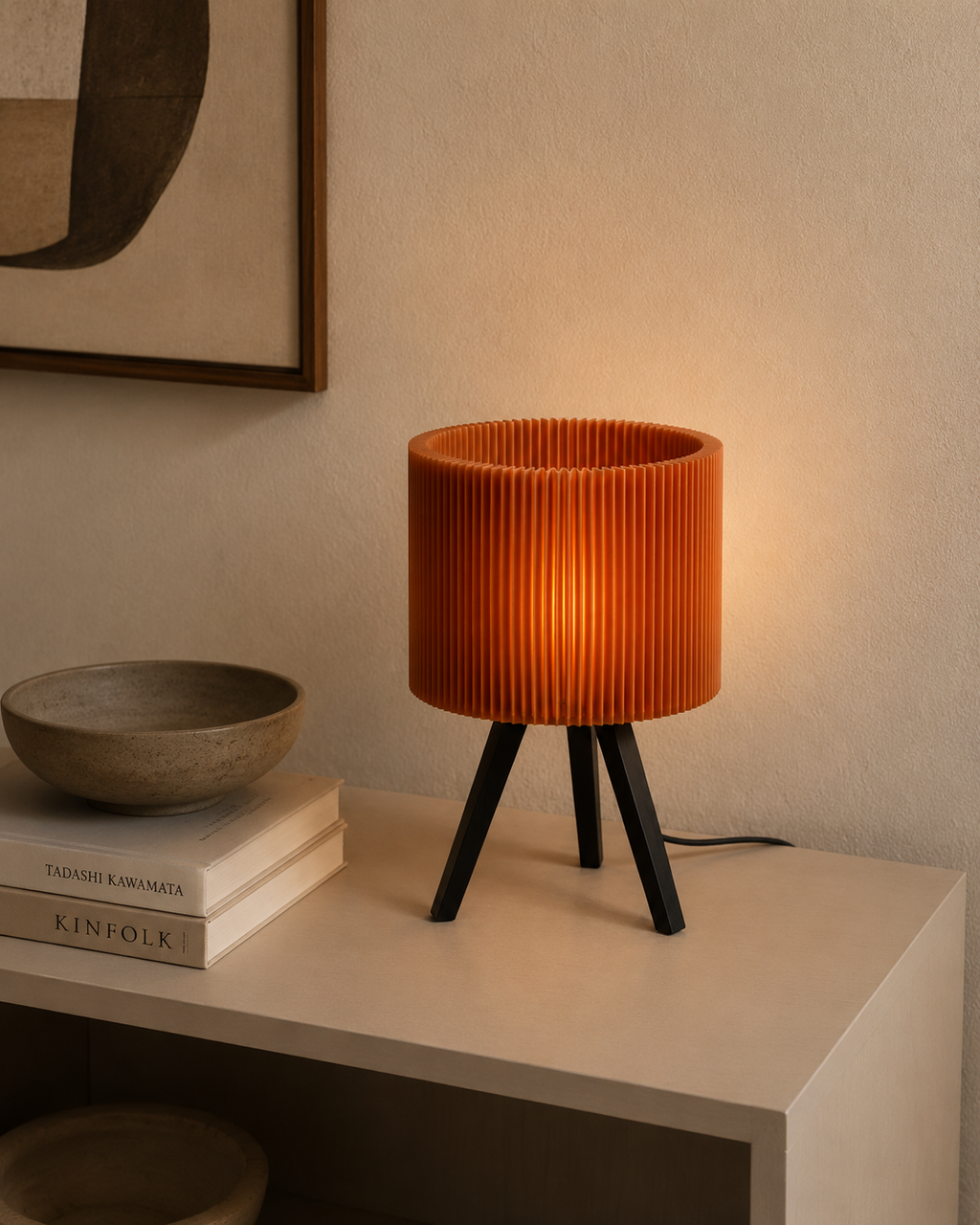 Pleated drum lamp on white shelf with books and ceramic bowl in moody setting