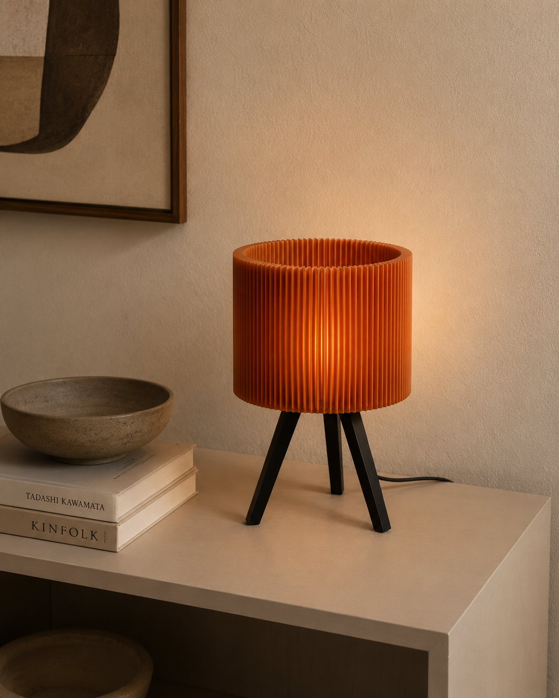 Pleated drum lamp on white shelf with books and ceramic bowl in moody setting